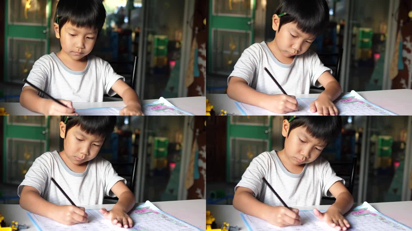 亚洲小男孩坐在课桌前写练习本。可爱的小学生在家里做作业，脸上带着微笑和专注。教育理念，学习，家校。