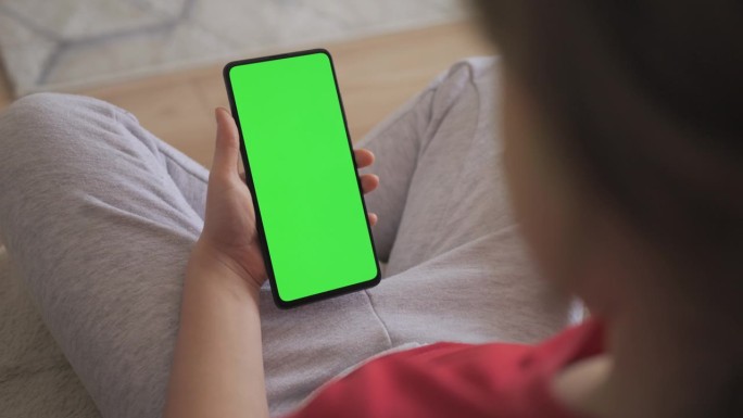 孩子在客厅使用绿色模型手机的视角。手机与绿色模拟屏幕色度键冲浪互联网观看内容视频博客学习。女孩在玩电
