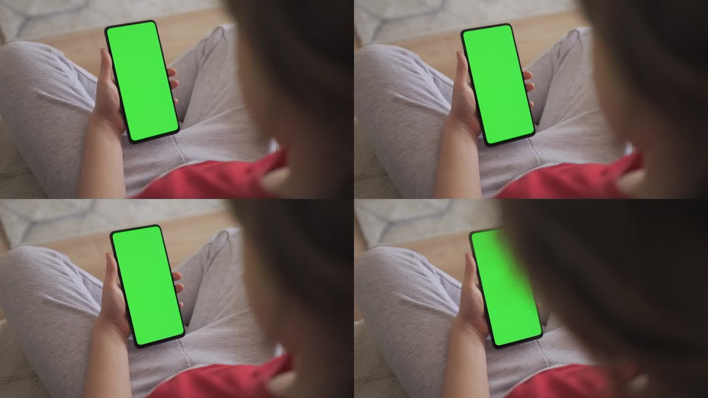孩子在客厅使用绿色模型手机的视角。手机与绿色模拟屏幕色度键冲浪互联网观看内容视频博客学习。女孩在玩电