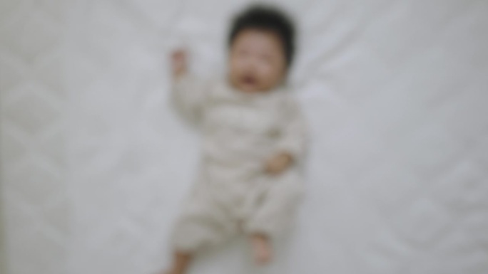 俯视图，一个刚出生的女婴穿着长袖婴儿服，仰面躺在床上蠕动。