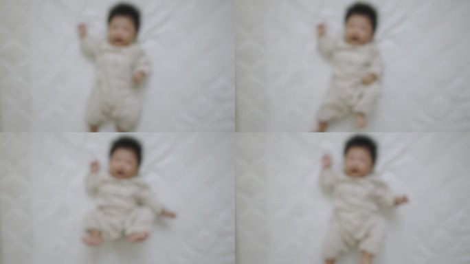俯视图，一个刚出生的女婴穿着长袖婴儿服，仰面躺在床上蠕动。