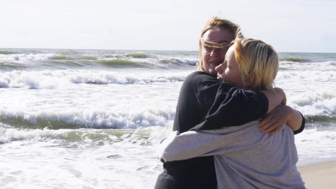美丽的母亲在大海的背景下拥抱着她心爱的女儿。