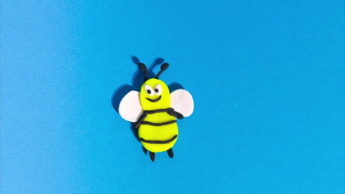 定格动画从橡皮泥。欢快有趣的蜜蜂在蓝色背景上飞翔