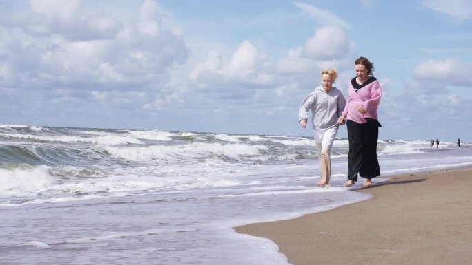 快乐的妈妈和女儿沿着海边在沙滩和水里奔跑。