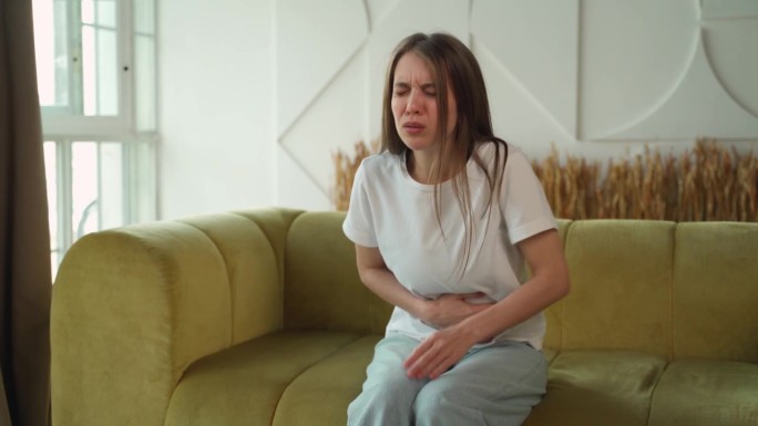 一名妇女坐在家里的沙发上时腹痛