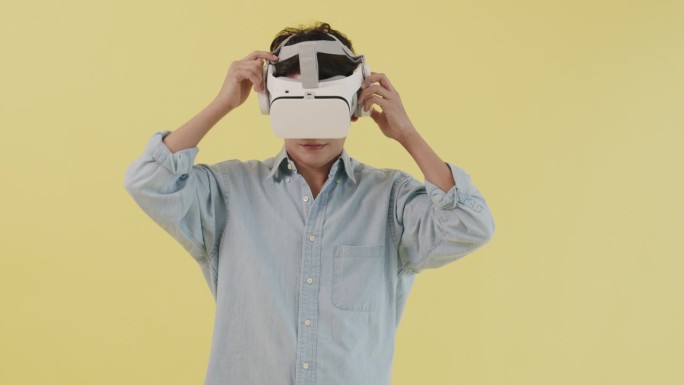 亚洲男性在摄影棚拍摄时使用虚拟或增强现实眼镜和未来娱乐，背景是黄色。
