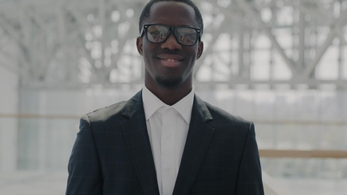 戴着眼镜和西装的非裔美国商人在办公室中心大厅微笑的慢动作肖像