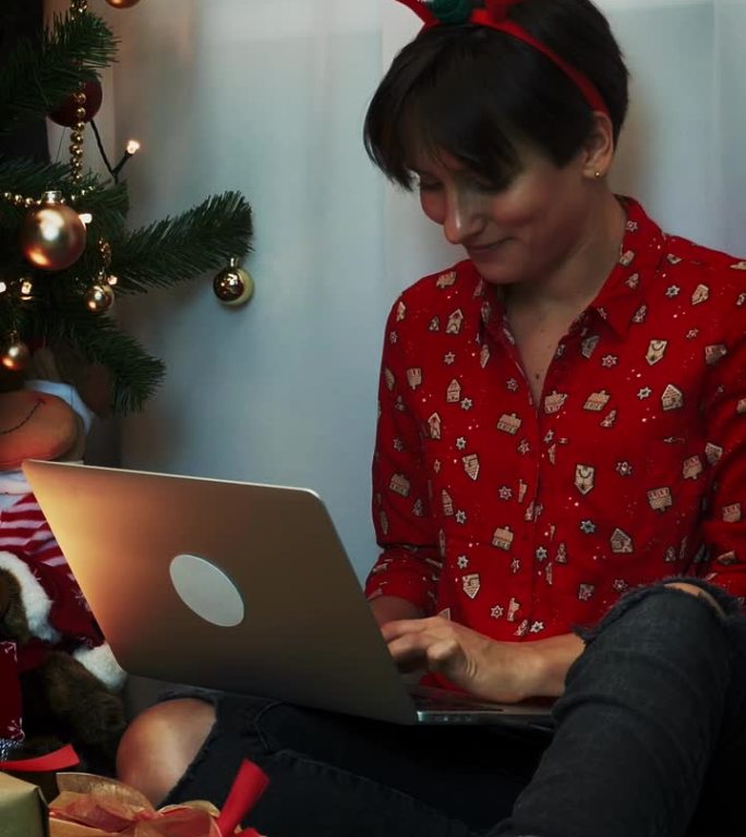 圣诞夜或新年夜，在笔记本电脑上工作的快乐女人。垂直视频
