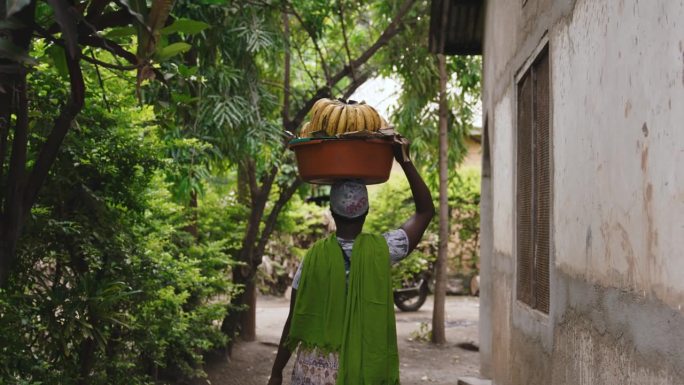 慢动作的女人在集装箱里搬运香蕉。拿着一串新鲜水果的女人。她在村子里散步。