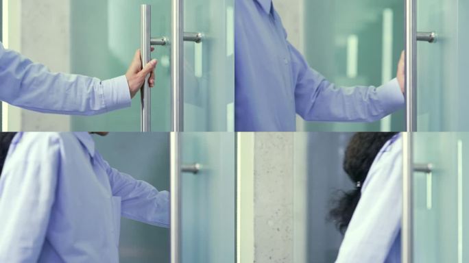近景:在一栋现代建筑中，一位女性手握着金属门把手打开办公室的玻璃门。