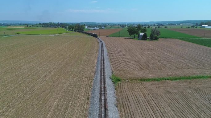 从空中俯瞰，一列蒸汽客运列车正驶近，穿过收获的农田