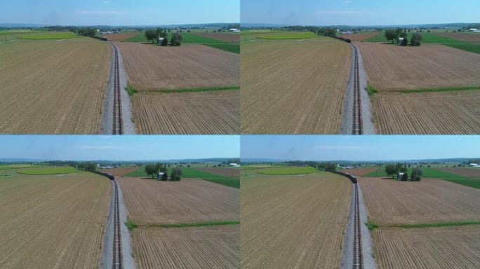 从空中俯瞰，一列蒸汽客运列车正驶近，穿过收获的农田