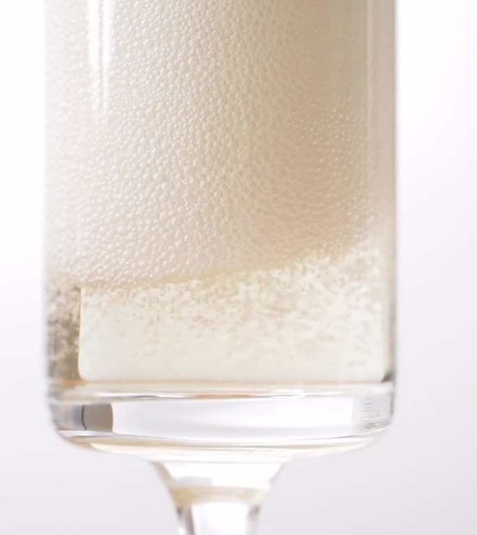 将香槟酒倒入一个透明的玻璃杯中，让许多气泡漂浮起来，奢华地散发着金色的光芒。