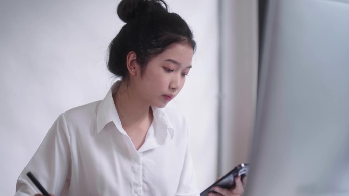 年轻的亚洲女性自由平面设计师或艺术家修图师，用触控笔在数字平板电脑上画画，看着电脑屏幕显示器，在她的