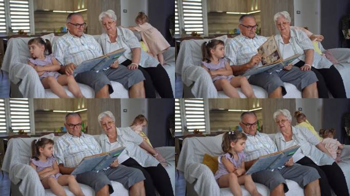 上了年纪的祖父母和大孙女坐在沙发上看相册，双胞胎小女儿在后面玩耍