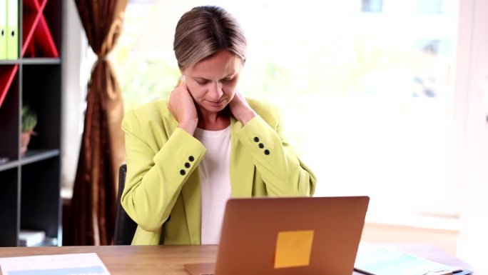 疲惫的女人在办公室里揉着僵硬酸痛的脖子和紧张的肌肉，因为她厌倦了在电脑前工作