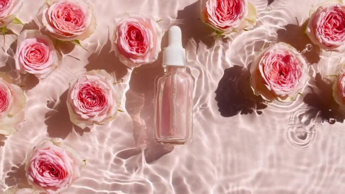 玻璃化妆瓶和粉色玫瑰花。缓慢运动的海浪。清澈的水与反射，折射阳光和阴影。天然的化妆品。设计、广告样品