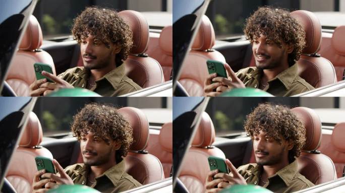 20多岁的男性司机坐在车里看手机。印度男子坐在敞篷车里玩智能手机。