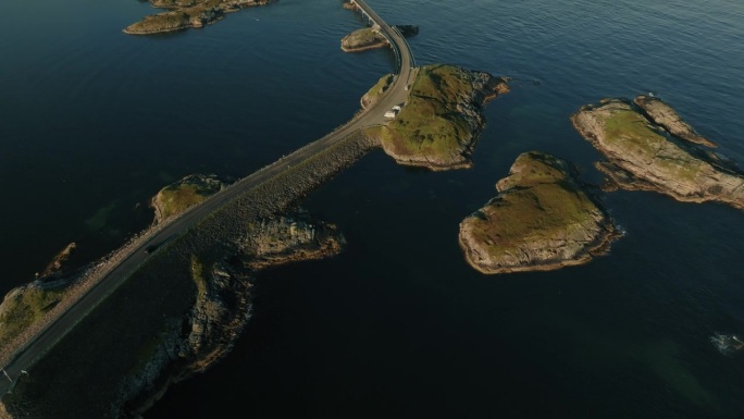 无人机在深蓝色的海面上飞行，露出长长的公路，在明亮的阳光下连接着小岩石岛屿
