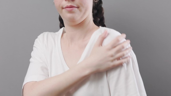 关节炎和软骨病。一位年轻女子用手按摩肩膀，感觉疼痛。演播室背景。健康保险的概念和韧带和关节的损伤