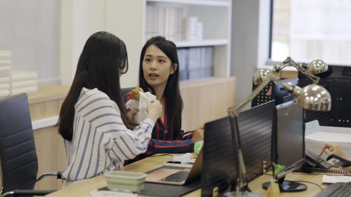 在公司的午休时间，两名女员工在办公室里吃饭聊天。