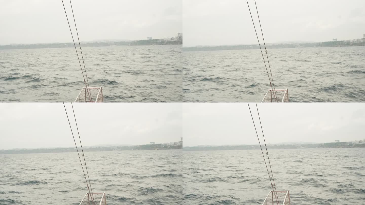 船首以汹涌的大海为背景，驶向城市。天气多云。