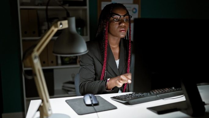一位专注的非裔美国女老板日夜管理着她的商业帝国，在办公桌前成功导航，在办公室电脑屏幕上掌握互联网