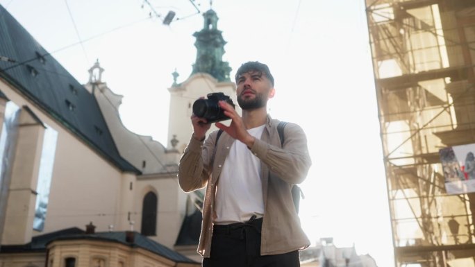 帅气的男摄影师在城市街道上用专业相机在阳光下拍照
