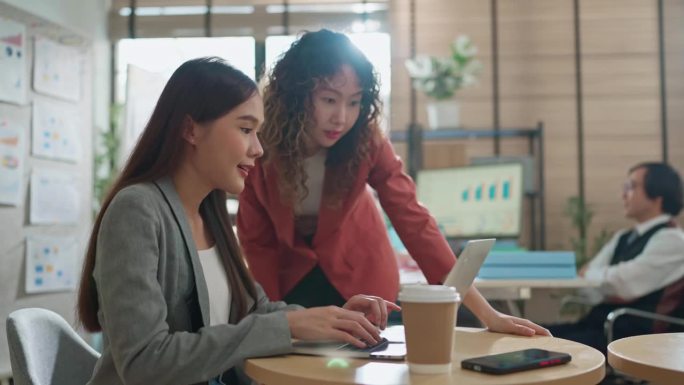 在一间现代化的办公室里，年轻的亚洲市场女性正坐在商务会议上。他们通过图表和笔记本电脑讨论一些事情，其