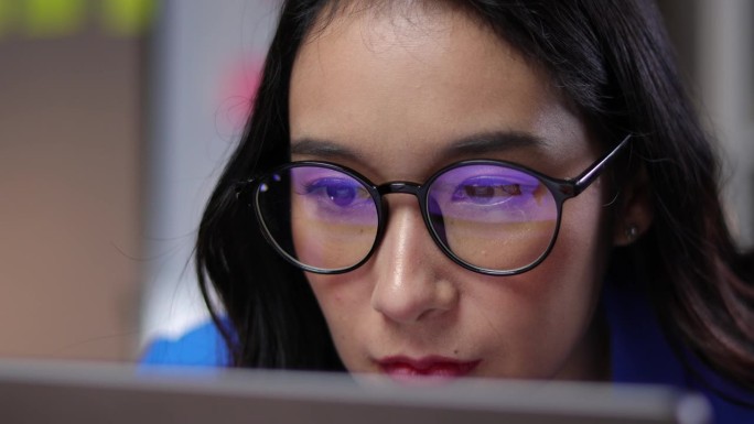 一个戴眼镜的女人目不转睛地盯着电脑屏幕的眼睛特写。严肃的女商人在办公室用电脑工作。
