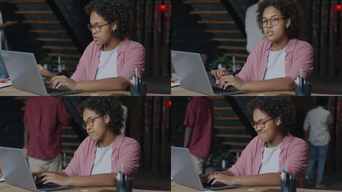 快乐的非裔美国女性办公室职员的肖像，在创造性的开放空间工作场所用笔记本电脑打字
