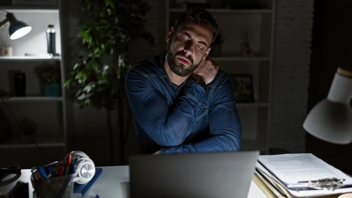 在昏暗的办公室里，年轻的西班牙裔商业工作者因过度劳累和压力而与腰酸背痛作斗争