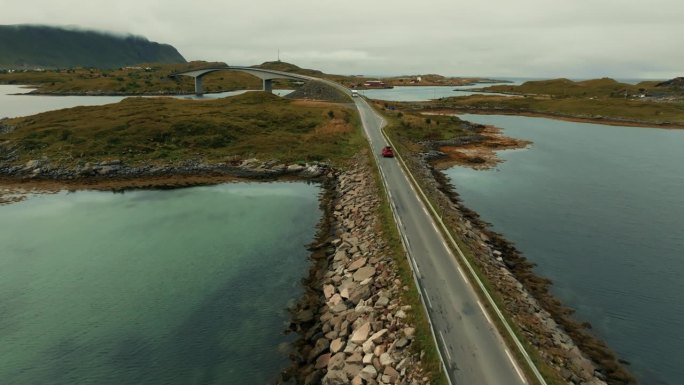 史诗般的斯堪的纳维亚全景。红色越野车行驶在绿色小岛之间的史诗般的道路上。