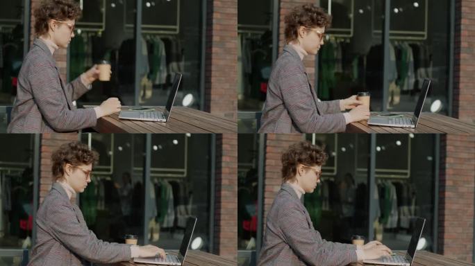 侧视图，自信的年轻女子使用笔记本电脑打字，喝咖啡，午休时间在街边咖啡馆工作