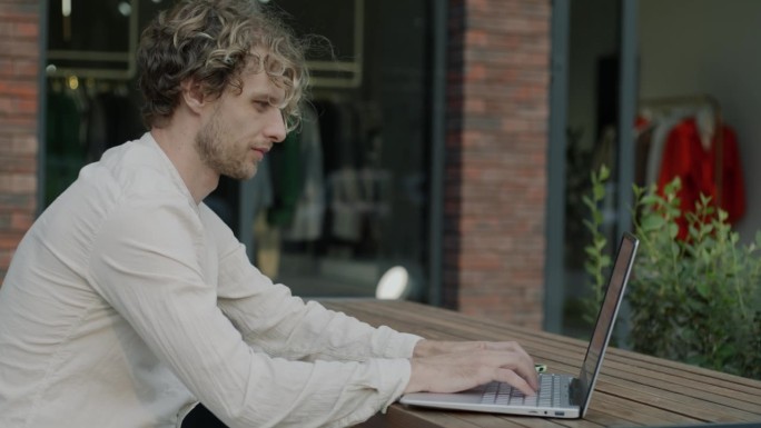 商人用手提电脑打字的侧视图，专注于街头咖啡馆的活动