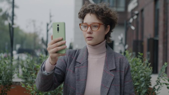 快乐的女学生在城市街道上用智能手机摄像头说话，挥手，进行在线视频通话