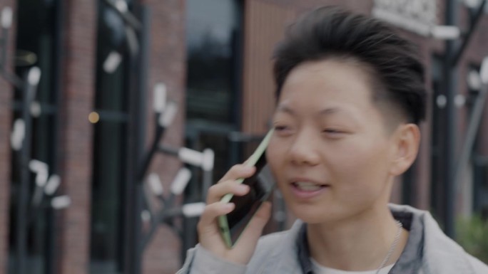 快乐的亚洲人走在城市街道上，用手机聊天，享受谈话的特写