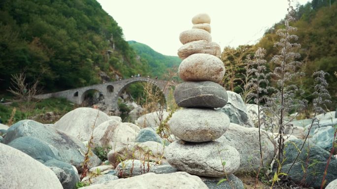 平衡与和谐。禅宗石和鹅卵石相互平衡地堆叠在一起，形成了一座塔，背景是一座石桥的拱门