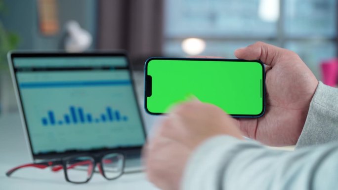 手机的特写与绿色的模拟屏幕在男人的手在桌面背景。男子轻触智能手机显示屏，显示课堂手势