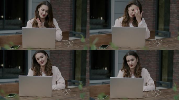 情绪化的年轻女子在街头咖啡馆用笔记本电脑进行在线视频通话