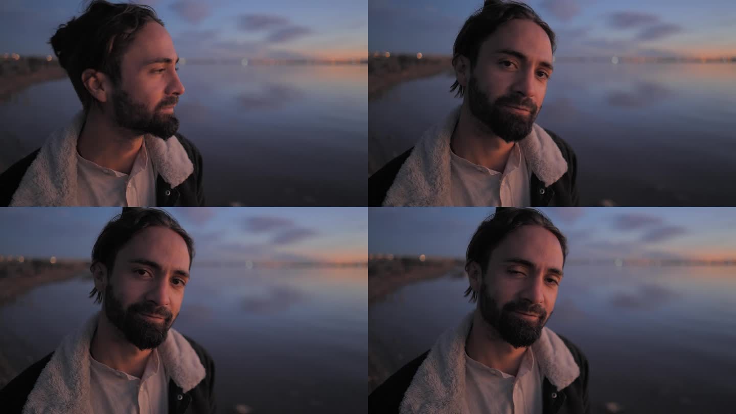一个英俊的大胡子男人在湖边欣赏日落，看着镜头，眨着眼睛，捋着胡子——慢动作