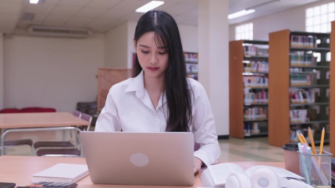 年轻的亚洲女大学生们正在用笔记本电脑认真地完成作业，在网上提交作业，参加网上课程，或在大学图书馆准备