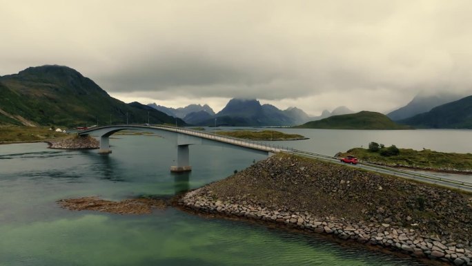 在史诗般的斯堪的纳维亚风景中，无人机跟随在桥上行驶的红色汽车。