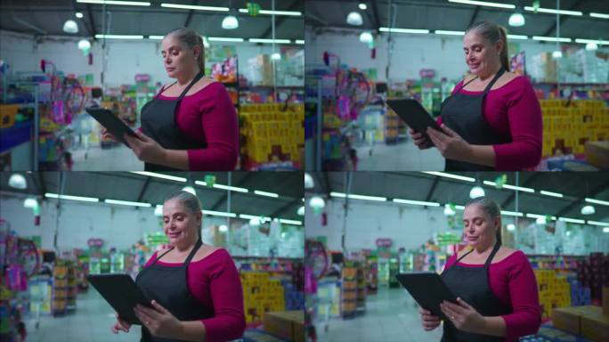 手持平板设备的连锁超市女企业家将情绪从中性转变为站在商业场内的快乐。中年妇女使用现代科技