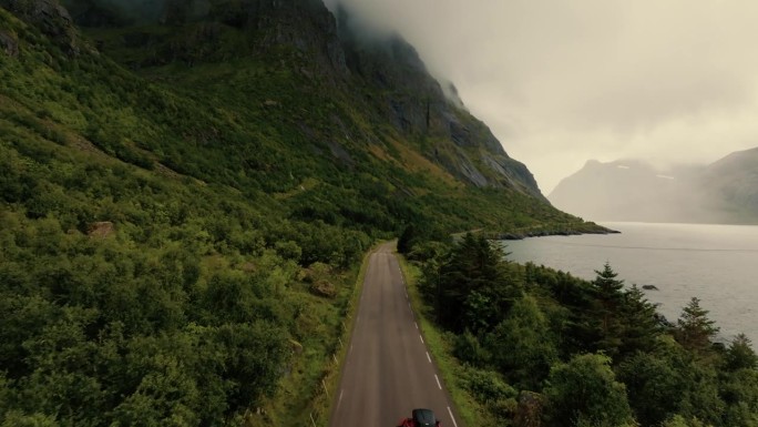 红色SUV行驶在美丽的绿色斯堪的纳维亚风景的沿海道路上