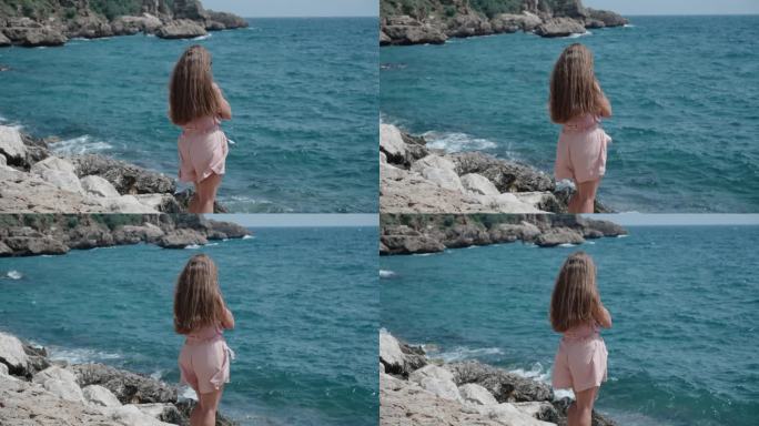 一个穿着粉色衣服的年轻女子站在海边的岩石上，她的长发和衣服在风中飘动，慢动作。