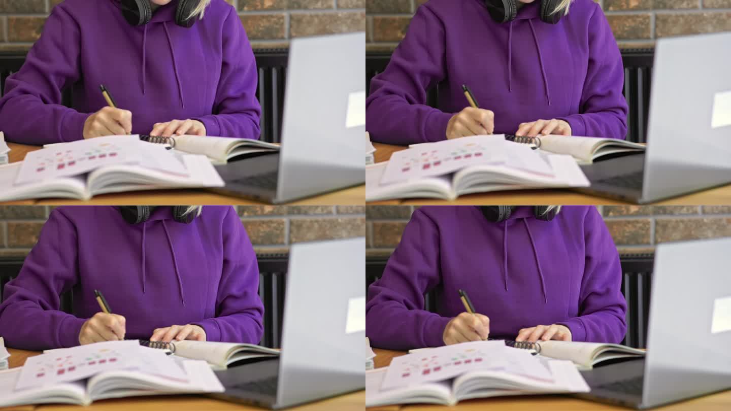 紫色衣服的女学生在写笔记，打开书，笔记本电脑放在桌子上