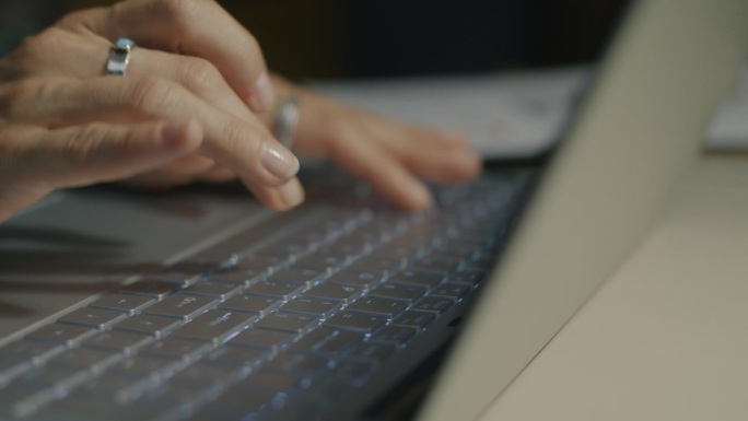 女性晚上在办公桌前工作时，用笔记本电脑键盘打字的特写
