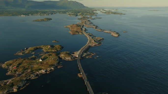 无人机将画面拉近，显示出大西洋公路，在明亮的阳光下连接着广阔的蓝色海洋中的小岛