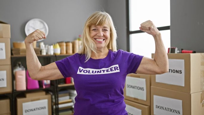 自信的中年金发女子热情地志愿服务，在慈善中心展示有力的手臂手势，微笑
